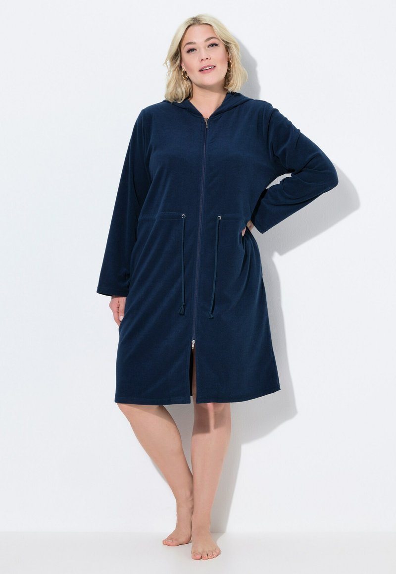 Tmavě modrý, zapínací, kapucínový župan vyrobený z měkké tkaniny. Obsahuje dlouhé rukávy, šňůrky na stažení a boční kapsy. Délka po kolena s rovnými nohavicemi.
