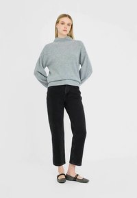 Sivý pletený sveter s vysokým golierom, čierne džíny s rovnými nohavicami a čierne baleríny. Jemná textúra; voľný strih; minimalistický dizajn.