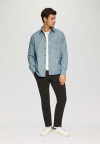 Lichtblauw, gestreept overhemd met knopen en een borstzak, gedragen over een wit t-shirt. Gecombineerd met zwarte broek en witte sneakers.