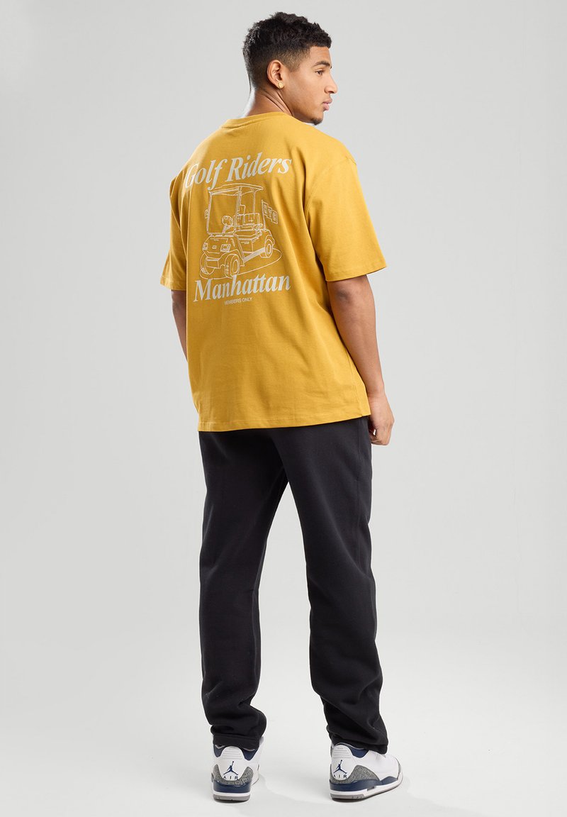 Yellow cotton t-shirt with short sleeves, featuring a graphic print of a golf cart and text on the back. Paired with black sweatpants.