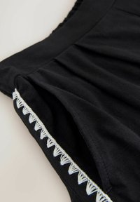 Tissu noir avec des surpiqûres décoratives blanches en forme de triangle le long du bord, montrant des plis et une texture lisse.