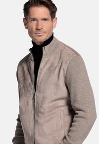 Beige zip-up jacket met een zachte suède-achtige voorkant en gebreide textuur mouwen. Voorzien van een hoge kraag en zijzakken.