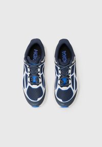 Des chaussures de sport bleues et blanches avec une tige en maille, un bout arrondi et une semelle texturée. Elles ont des lacets bleus et un logo sur la languette.