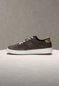 Rjavi sintetični športni copati z geometričnim vzorcem logotipa, belim podplatom in zlatim poudarkom na peti. Imajo bele vezalke in gladko teksturo.