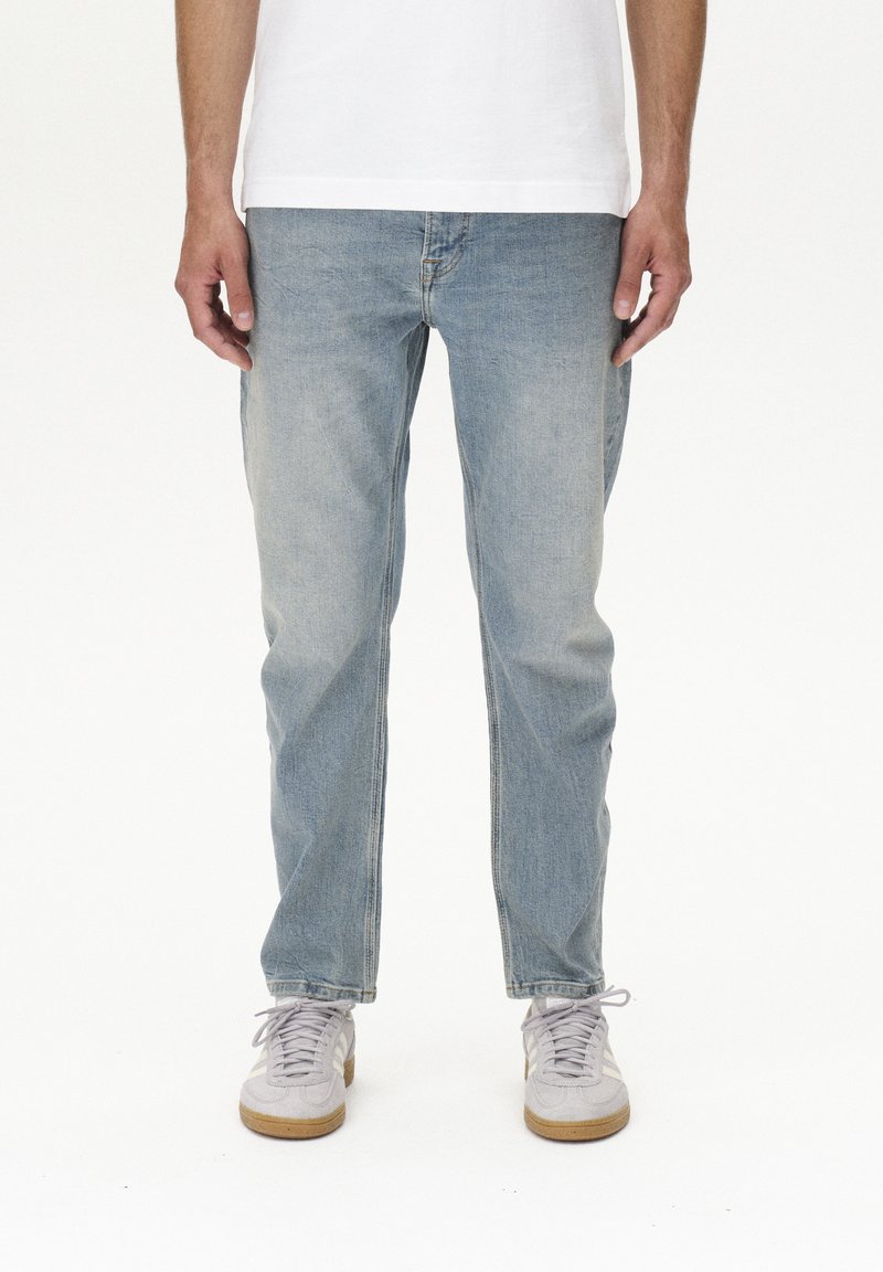 Vaqueros de denim azul claro con ajuste recto, textura desgastada y costuras mínimas. Combinados con zapatillas grises con un acento blanco.