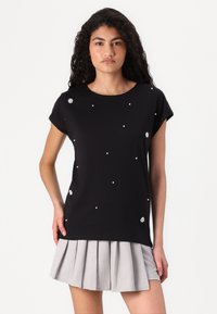 Black t-shirt with short sleeves, adorned with white pearl-like details and a floral accent on the side, paired with a gray pleated skirt.