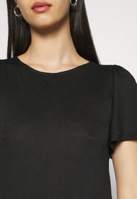 Haut noir à manches courtes avec un col rond. Texture côtelée, manches légèrement bouffantes et silhouette ajustée.