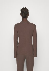 Haut long à manches ribbées marron avec col rond et design ajusté, doté d'un tissu texturé et d'un dos sans couture.