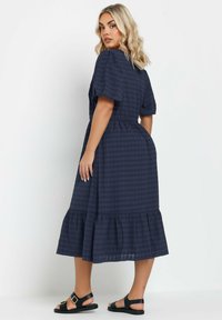 Laivansininen ruudullinen midi-mekko puffihihnoilla, vyötäröltä kapeana ja kerroksellisella rypytyshelman. Yhdistetty mustiin litteisiin sandaaleihin.