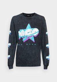 Černé tričko s dlouhým rukávem vyrobené z bavlny, které má texturovaný grafický potisk se vzorem modrých a fialových hvězdiček a textem na přední straně a rukávech.