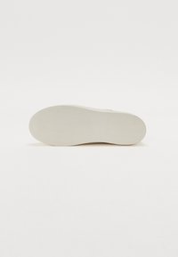 White sneaker sole with textured rubber for grip, oval shape, smooth finish, and raised zigzag pattern in the center and toe area.