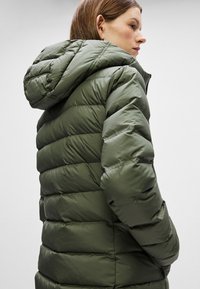 Chaqueta acolchada verde con capucha, con un diseño acolchado y un acabado brillante. Las mangas están ligeramente fruncidas en los puños.