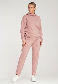Różowa bluza z kapturem o luźnym kroju, w zestawie z dopasowanymi spodniami o tapered fit z kieszeniami. Uzupełniona białymi trampkami. Gładka tekstura materiału.