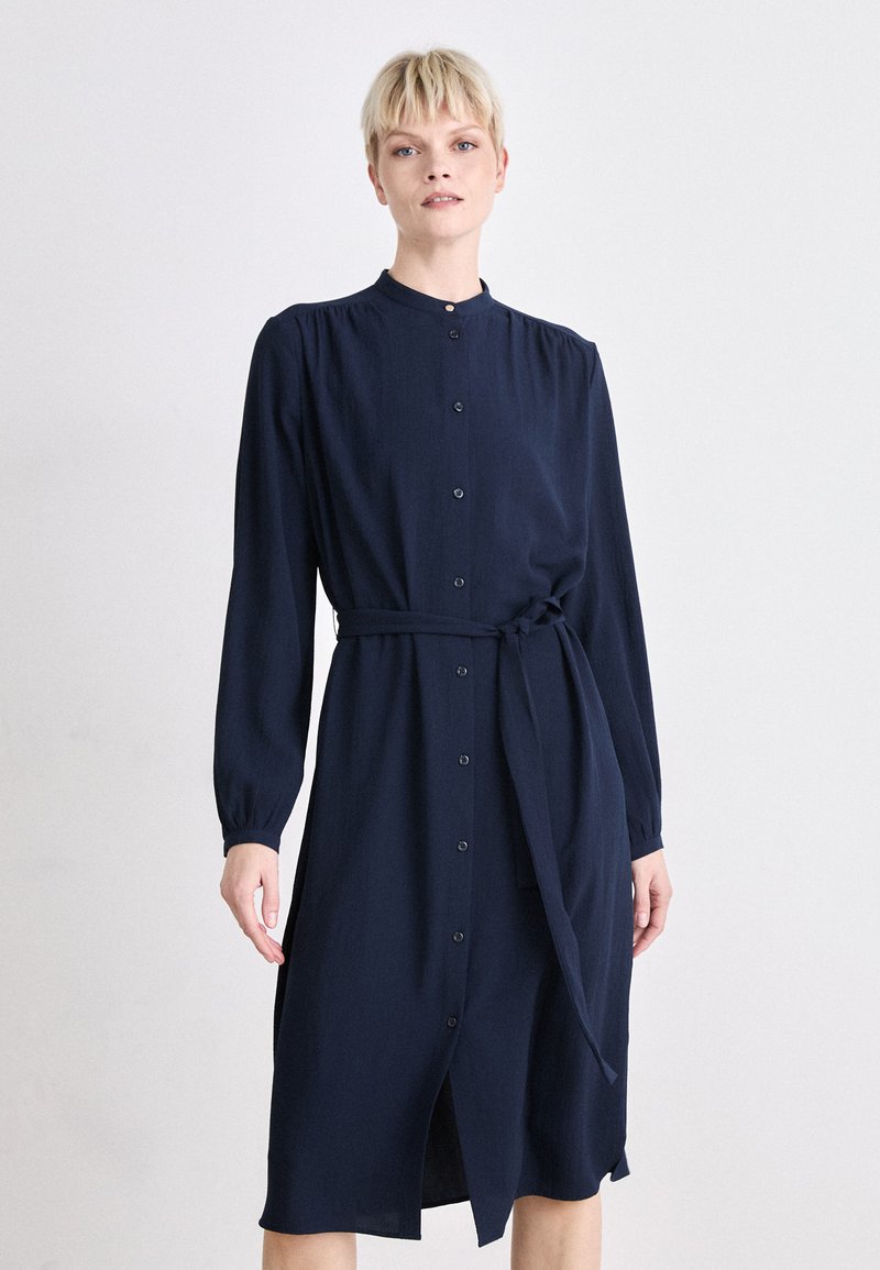 Navy button-up dress with long sleeves, a collar, and a tie waist. Made from a smooth fabric, featuring a straight cut and knee-length hem.