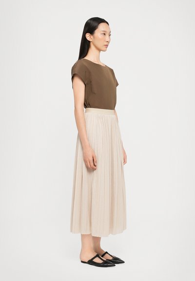 Braunes Kurzarmoberteil, beiges plissiertes Midi-Rock und schwarze flache Schuhe mit Riemen. Glatte Texturen, schlichtes Design und neutrale Farben.