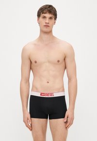 Boxer aderenti neri con fascia elastica rossa e bianca con logo "DIESEL", vestibilità aderente, tessuto liscio, lunghezza a metà coscia.