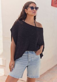 Top oversized in crochet nero con maniche corte, abbinato a pantaloni shorts in denim azzurro chiaro, con un taglio classico e un leggero effetto sbiadito.