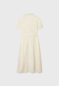 Kremowa lniana sukienka z krótkimi rękawami, kołnierzykiem i paskiem w talii. Tył ma środkowy szew i prostą, swobodnie opadającą sylwetkę.