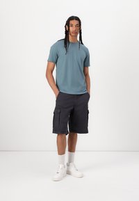 T-shirt de algodão azul claro combinado com calções de carga escuros com bolsos laterais. Modelo a usar sapatilhas brancas com meias até ao tornozelo.