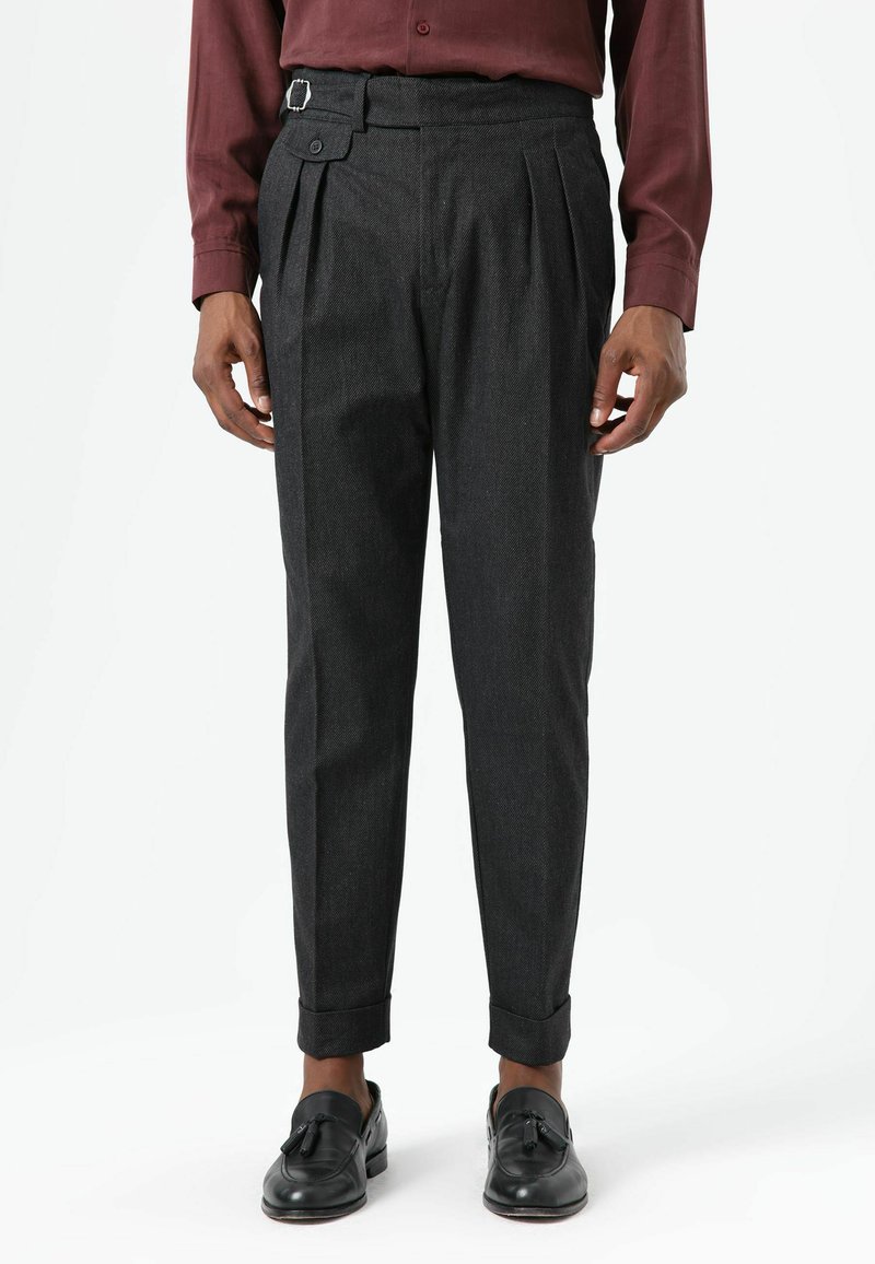 Grijze geplooide broek met een riem en een vierkante gesp, taps toelopende pijp en omgeslagen zoom, gecombineerd met zwarte instapschoenen.