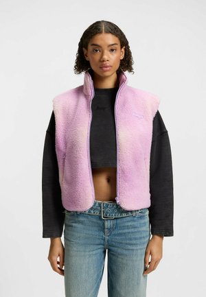 Fleece vest in gradient pink with a high collar and zip closure. Features short sleeves and a soft, textured finish.