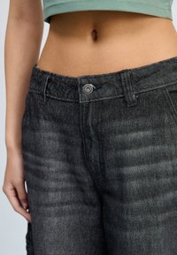 Black denim pants with a textured finish, featuring a front button closure and belt loops, shown with a cropped top above the waistline.