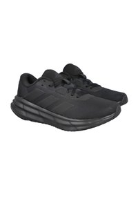 Zapatos deportivos negros con parte superior de malla, suela acolchada y tres franjas como detalles. Presentan puntera redondeada y diseño con cordones.