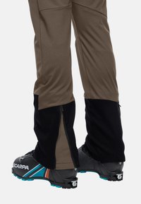 Bruine en zwarte outdoor broek met zijritsen, gecombineerd met zwarte skibotten met kleurrijke accenten en een gestructureerde zool.