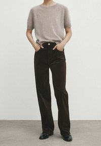 Haut en tricot marron clair à manches courtes associé à un pantalon en velours côtelé marron foncé. Les pantalons ont des poches avant et une coupe droite. Chaussures noires.