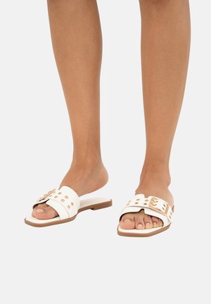 Chanclas blancas con suela plana, decoradas con tachuelas en tono dorado y una correa ancha. El diseño es minimalista y tiene la punta abierta.