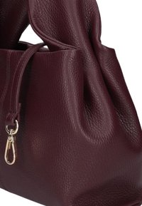 Bordeaux lederen handtas met een gestructureerde afwerking, voorzien van een gedraaide handgreep en een gouden clip voor extra detail. Zachte, ronde vorm.