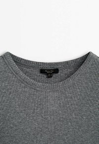 Gros plan d'un t-shirt gris en maille côtelée à col rond avec une étiquette noire Massimo Dutti cousue à l'intérieur du col.