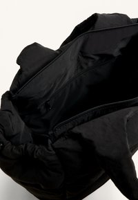 Fekete steppelt táska, puha külsővel, cipzáras belső zsebekkel és felső nyílással. Kerek formával és texturált anyaggal rendelkezik.