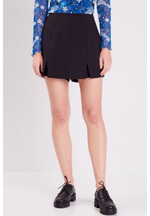 Jupe-culotte noire avec un design plissé, fabriquée en tissu léger. Associée à des chaussures noires à lacets et un haut à manches longues à motifs bleus.