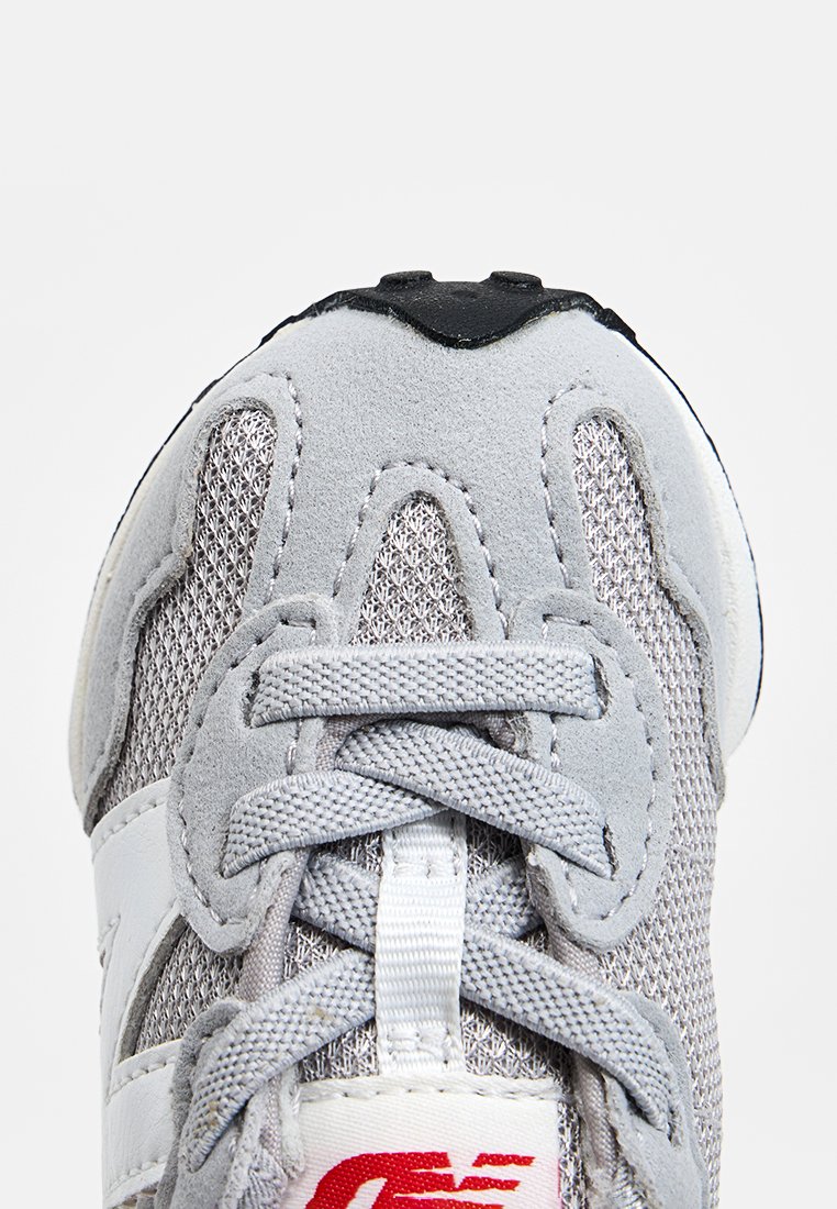 Baskets grises en matériaux mesh et suède, avec des accents blancs, des lacets ronds et un logo rouge. Semelle texturée avec un embout arrondi.