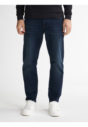 Mørkeblå jeans lavet af denim med lige ben. Sammen med hvide sneakers, der har et enkelt design og rund tå.