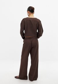 Rjav skrajšan dolg rokav top z širokim izrezom, v kombinaciji z ohlapnimi rjavimi hlačami. Gladek, lahkoten material z elastiko v pasu.