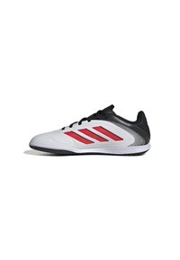 Zapatilla deportiva blanca con acentos negros y diseño de rayas rojas. Presenta una parte superior suave, puntera redondeada y suela negra texturizada para tracción.