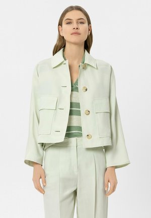 Woman wearing light green buttoned cropped jacket over green and beige striped top and matching light green high-waist pants.