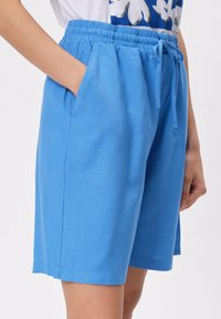 Jasnoniebieskie szorty z bawełny, z elastycznym paskiem w talii i sznurkiem, dwiema bocznymi kieszeniami oraz prostym krojem.