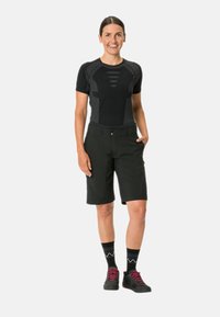 Top negro de manga corta con acentos texturizados, combinado con pantalones cortos negros a la altura de la rodilla. El modelo lleva calcetines a rayas en blanco y negro y zapatos negros.