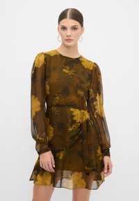 Bruine jurk met bloemenprint en lange doorzichtige mouwen, met een striktaille en een gelaagde zoom. Gele en zwarte bloemenpatronen op een doorschijnende stof.