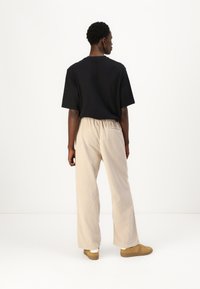 Black cotton t-shirt and beige corduroy pants with an elastic waistband, featuring a back pocket and a relaxed cut. Light brown shoes.