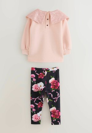 Maglietta a maniche lunghe rosa chiaro con colletto di paillettes, abbinata a leggings neri con stampa floreale colorata e dettagli in raso.