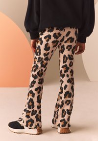 Utsvängda byxor i ribbad tyg med beige bas och svart- och brunt leopardmönster. Matchade med svarta sneakers med vit sula.