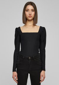 Svart ribbet body-suit med firkantet utringning og lange puff-ermer, kombinert med svarte høyt midje bukser. Glatt tekstur og tettsittende design.