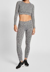 Conjunto de ropa deportiva en gris claro que incluye un top corto de manga larga y leggings de cintura alta con patrones abstractos en gris oscuro, combinado con zapatillas negras.
