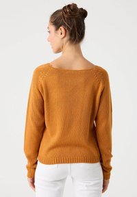 Suéter de color óxido con un escote amplio, mangas largas y dobladillo acanalado. Textura suave y detalle de punto en las costuras de los hombros.