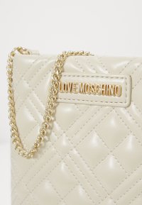 Borsa beige trapuntata realizzata in pelle liscia, con una tracolla in catena dorata e un logo "LOVE MOSCHINO" dorato su una toppa rettangolare.