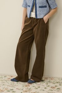 Hnedé kordurové nohavice širokého strihu s bočnými vreckami, v kombinácii s modrými textilnými papučami a textúrovanou modrou bundou. Kvetinový vzor na podlahe.